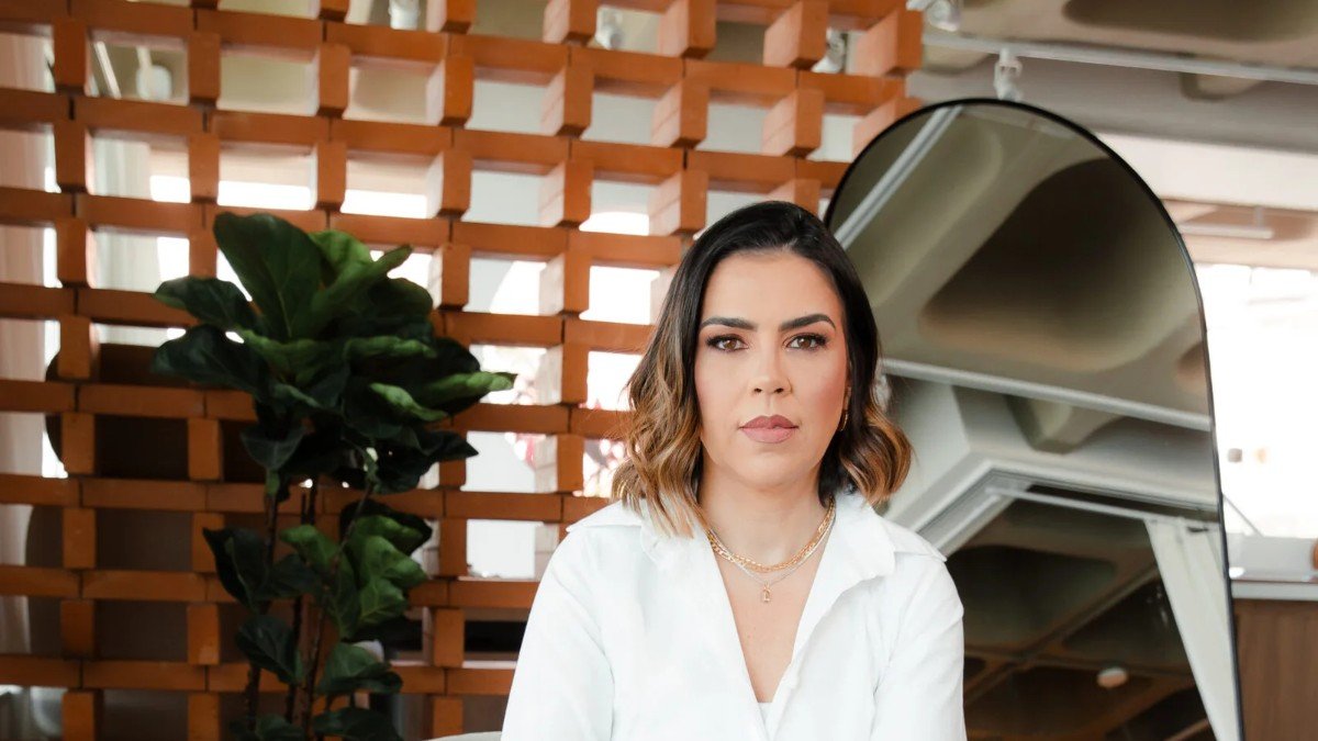 Luciana Prates, de camisa branca, sentada em um ambiente de trabalho iluminado